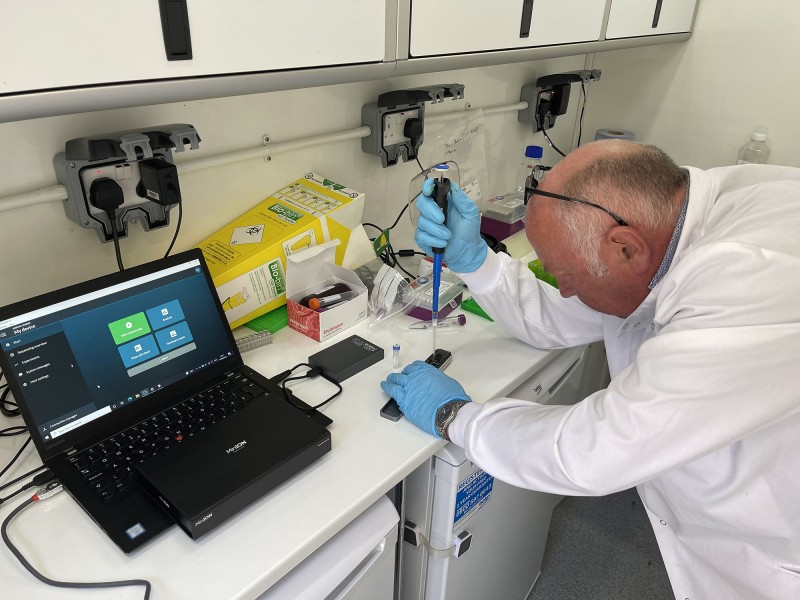 A male Hub colleague uses water sampling equipment on a workbench in the lab in a van